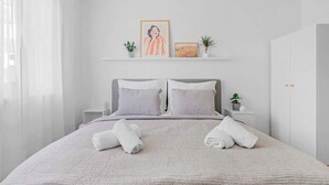 Une chambre à coucher bien rangée, avec un lit, des oreillers, une table de chevet, une petite plante et un tableau encadré au mur.