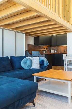 Een moderne woonkamer met een blauwe bank, een houten salontafel, en een keuken met donkere kastjes en een werkblad.