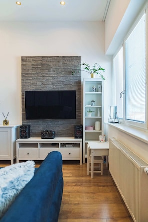 Een moderne woonkamer met een flatscreen-tv, een wand met stenenstructuur, een wit wandrek en een raam met zonwering.
