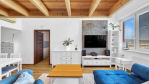 Uma sala de estar moderna com teto de madeira, paredes brancas, lareira de pedra, televisão de tela plana e sofás azuis.