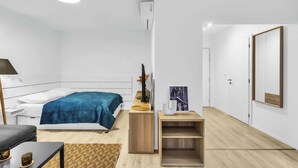 Ein modernes, minimalistisches Schlafzimmer mit Bett, Nachttisch, Lampe und einer kleinen Holzablage.