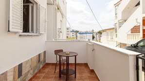 Un balcón con mesa y sillas, paredes blancas y vistas a edificios.
