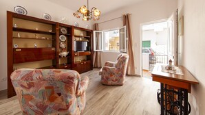 Una sala de estar con un aparador de madera, sillones estampados, un televisor y una araña.