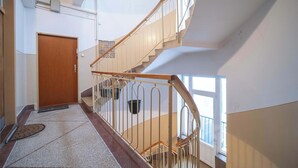 A multi-level interior with a wooden door, a metal staircase with a handrail, and a window allowing natural light. - Your City Center Stylish & Spacious Apartment (Košice)