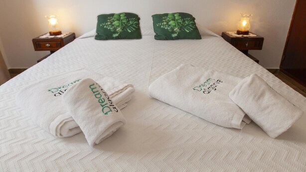 Un letto ben rifatto con due cuscini e due asciugamani piegati, ognuno con un logo verde.