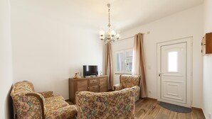 Un soggiorno con televisione, poltrone a motivi floreali, un armadietto in legno e un lampadario.