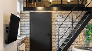 Uma cozinha moderna com parede de tijolos, porta preta, mesa de jantar de madeira e escada com guarda-corrimão de metal.