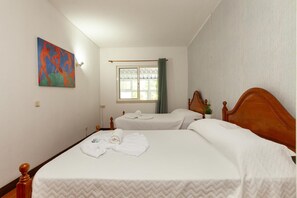 A hotel room with two beds, a window with curtains, a painting on the wall, and a small plant on the bedside table. - A72 - Praia da Luz Coast Flat (Praia da Luz)