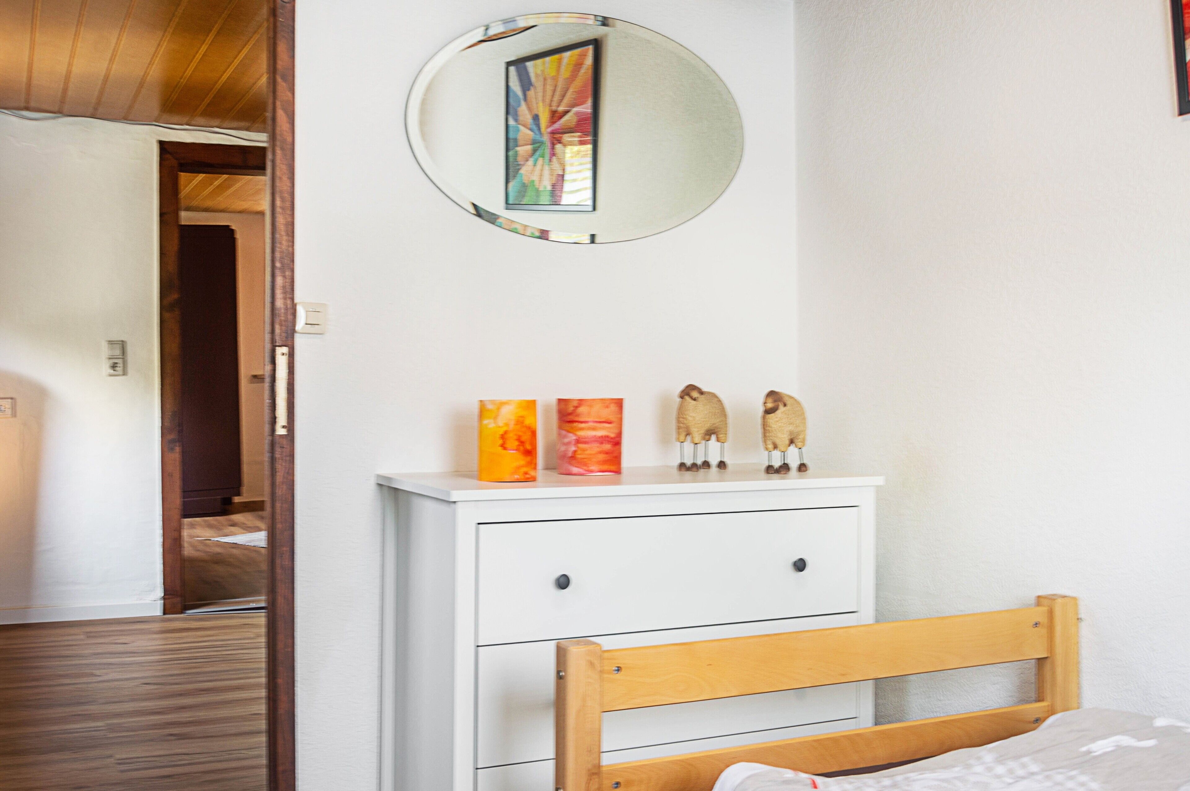 A bedroom with a wooden bed, a white dresser, a mirror, and a door leading to another room.