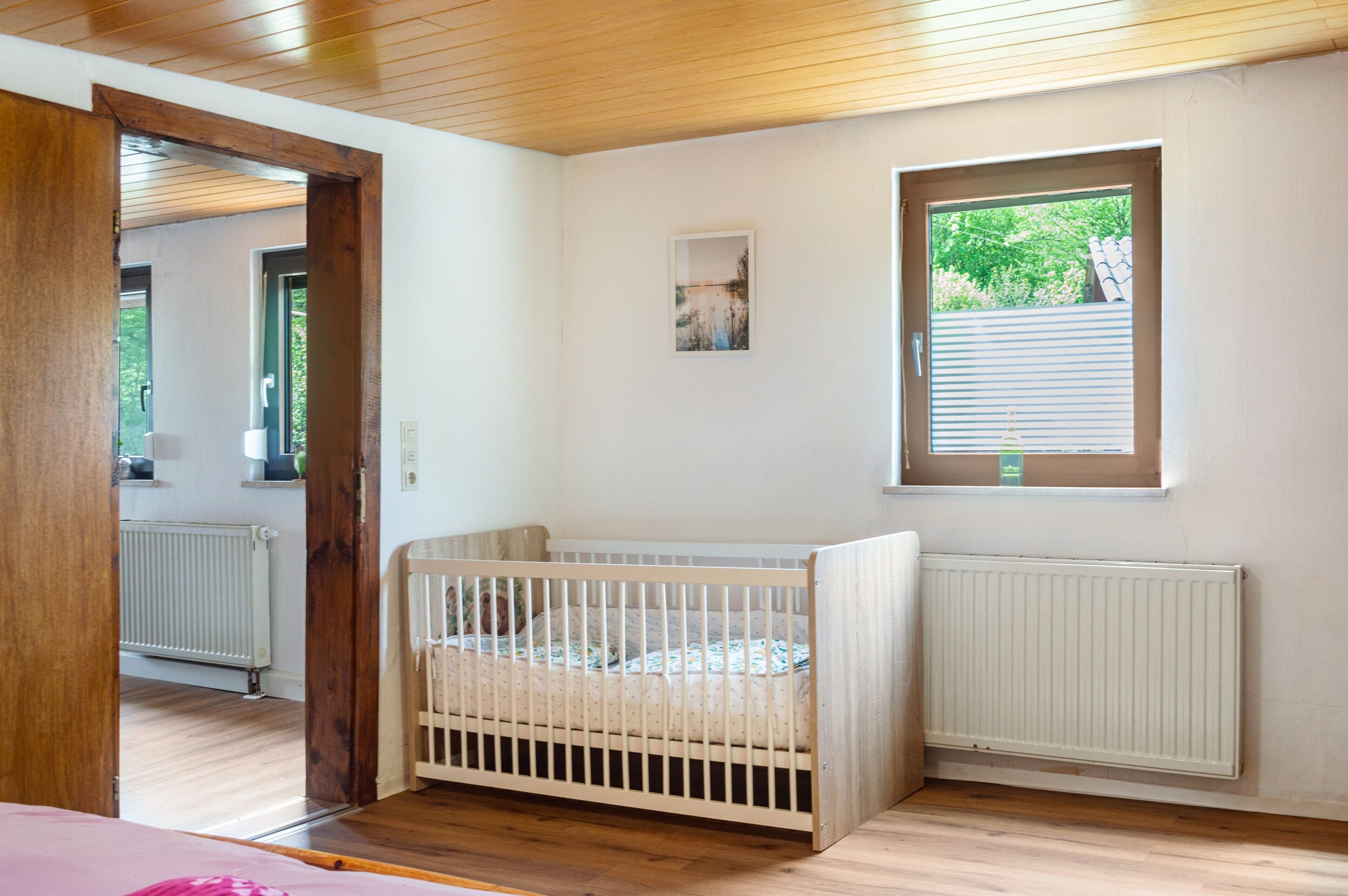 Ein Zimmer mit Babybett, Fenster und Heizkörper.