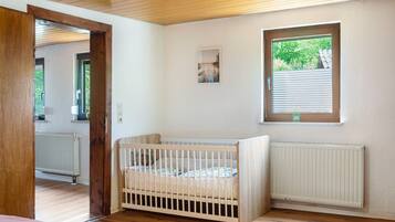 Ein Zimmer mit Babybett, Fenster und Heizkörper.