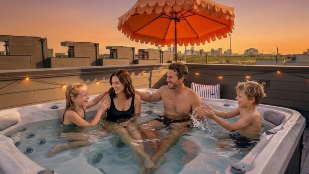 A hot tub with four people, an umbrella, and a city skyline in the background.