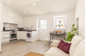 Un espacio habitable compacto con kitchenette, lavadora, comedor con mesa y sillas, y sofá con cojín.