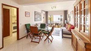 A dining area with a glass table, wooden chairs, a sofa, and a cabinet with glass doors. - A02 - Casa Topazio in Quarteira (Quarteira)
