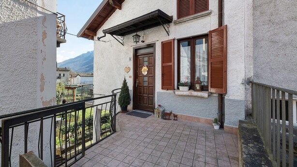 A building with a balcony, a door with a doormat, and a small garden area.