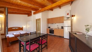 A compact hotel room with a wooden ceiling, a bed, a small kitchenette, and a dining area.