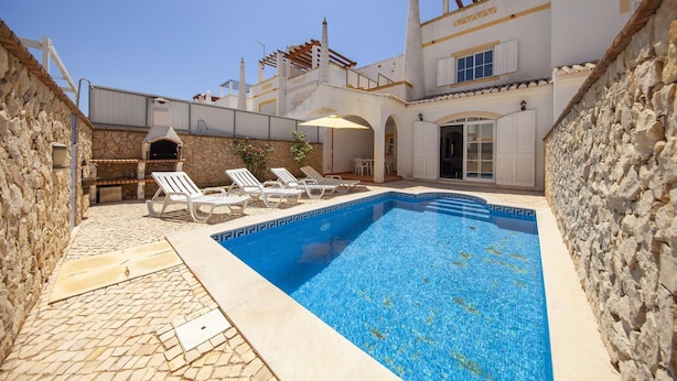 A swimming pool with lounge chairs, a stone wall, and a building with a white facade and arches. - FF 01 - Bedroom 1 in Sea Breeze Guesthouse (Lagos)