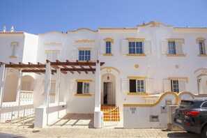 Un edificio blanco con detalles amarillos, un acceso cubierto y un automóvil estacionado en la parte delantera.