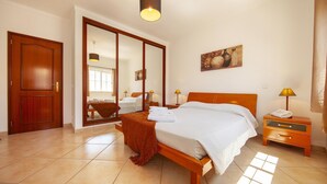 A hotel room with a bed, a nightstand, a lamp, a mirror, and a door. - FF 01 - Bedroom 1 in Sea Breeze Guesthouse (Lagos)