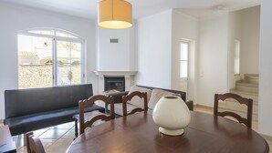 A dining area with a round table, chairs, a vase, a sofa, a fireplace, and a view through a window.