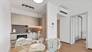 A modern kitchen with a glass dining table, wooden chairs, and a built-in oven. - Eurovea Tower Apt 1 Danube View (Bratislava)