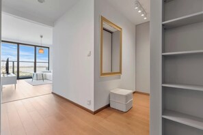 Ein modernes Hotelzimmer mit großem Fenster, einem Spiegel, einer kleinen weißen Bank und einer eingebauten Regallösung.