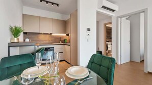Une cuisine moderne dotée d’appareils électroménagers intégrés, un coin repas avec une table en verre et des chaises recouvertes d’un tissu vert.