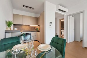 A modern kitchen with built-in appliances, a dining area with a glass table, and green upholstered chairs. - Eurovea Tower Apt 2 Sky View (Bratislava)