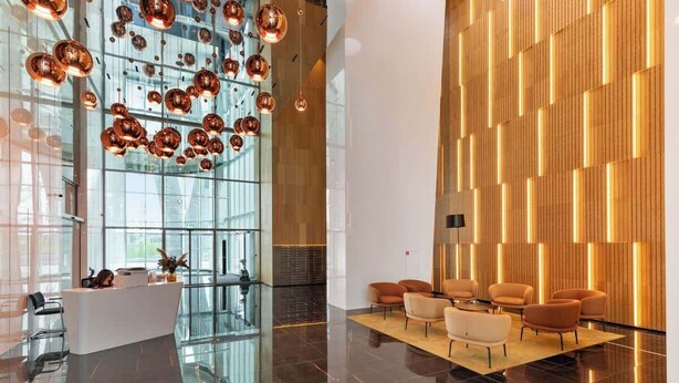 Un hall d’entrée moderne avec un comptoir d’accueil, des murs en verre et un espace détente doté de fauteuils orange.