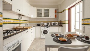 A compact kitchen with a gas stove, microwave, and washing machine, a dining table with a meal set, and a window with a view.
