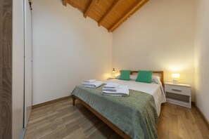 A bedroom with a wooden ceiling, a bed with a green bedspread, two pillows, a nightstand with a lamp, and a door on the left. - A28 - Castela Street Townhouse in Espiche (Praia da Luz)