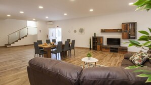Amplia sala de estar con mesa de comedor, sofás, televisor y una escalera.
