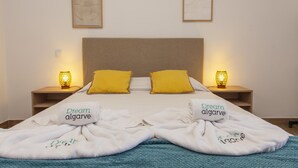 Una cama bien hecha con dos almohadas, dos lámparas de noche y dos cuadros en la pared.