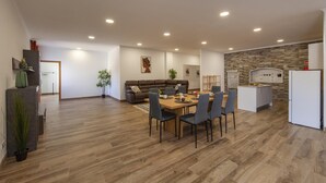 A modern kitchen with a built-in oven, a dining area with a wooden table and chairs, and a living room with a sofa and a painting on the wall.