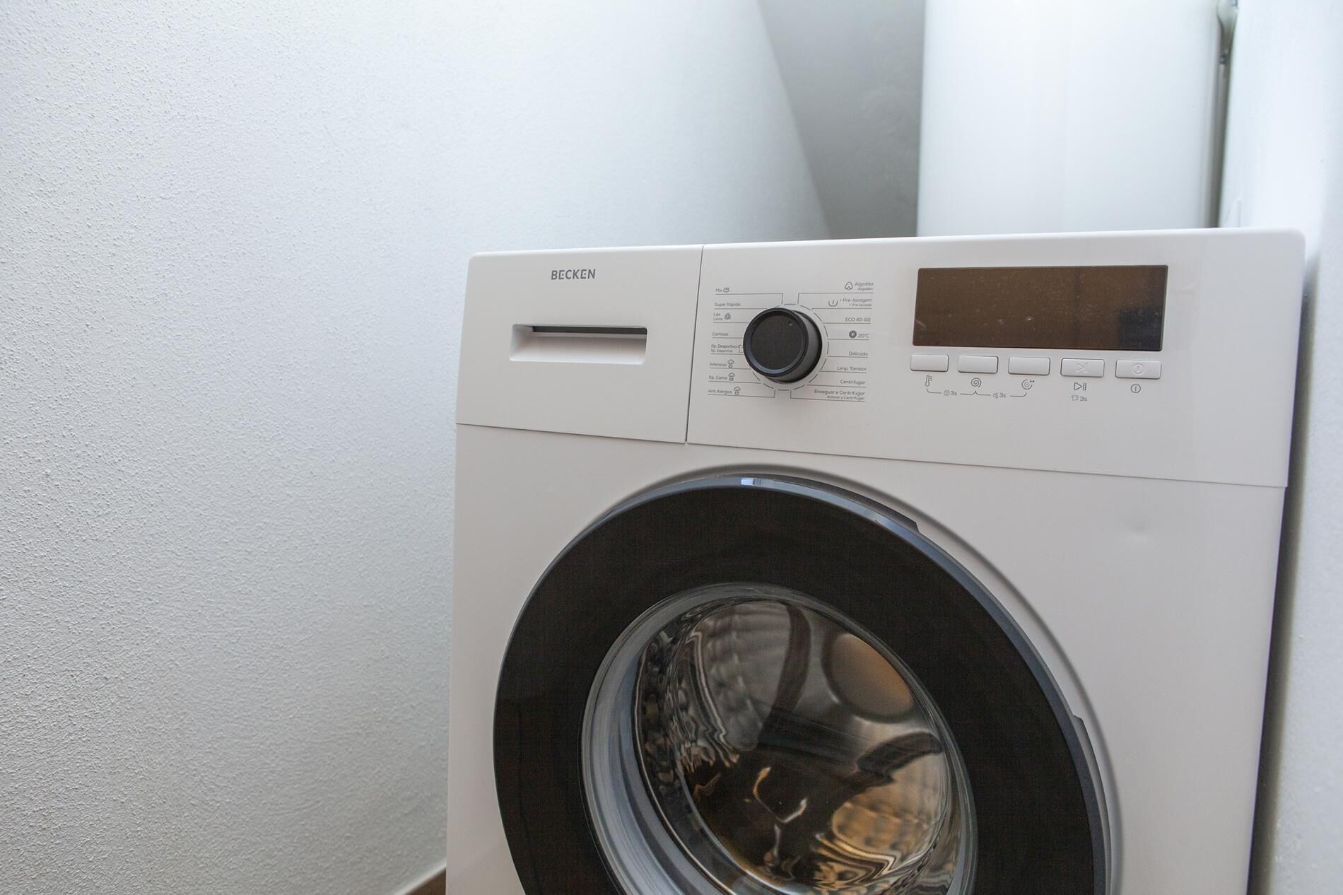 A front view of a white, wall-mounted, front-loading washing machine with a control panel and a digital display.