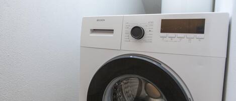 A front view of a white, wall-mounted, front-loading washing machine with a control panel and a digital display.