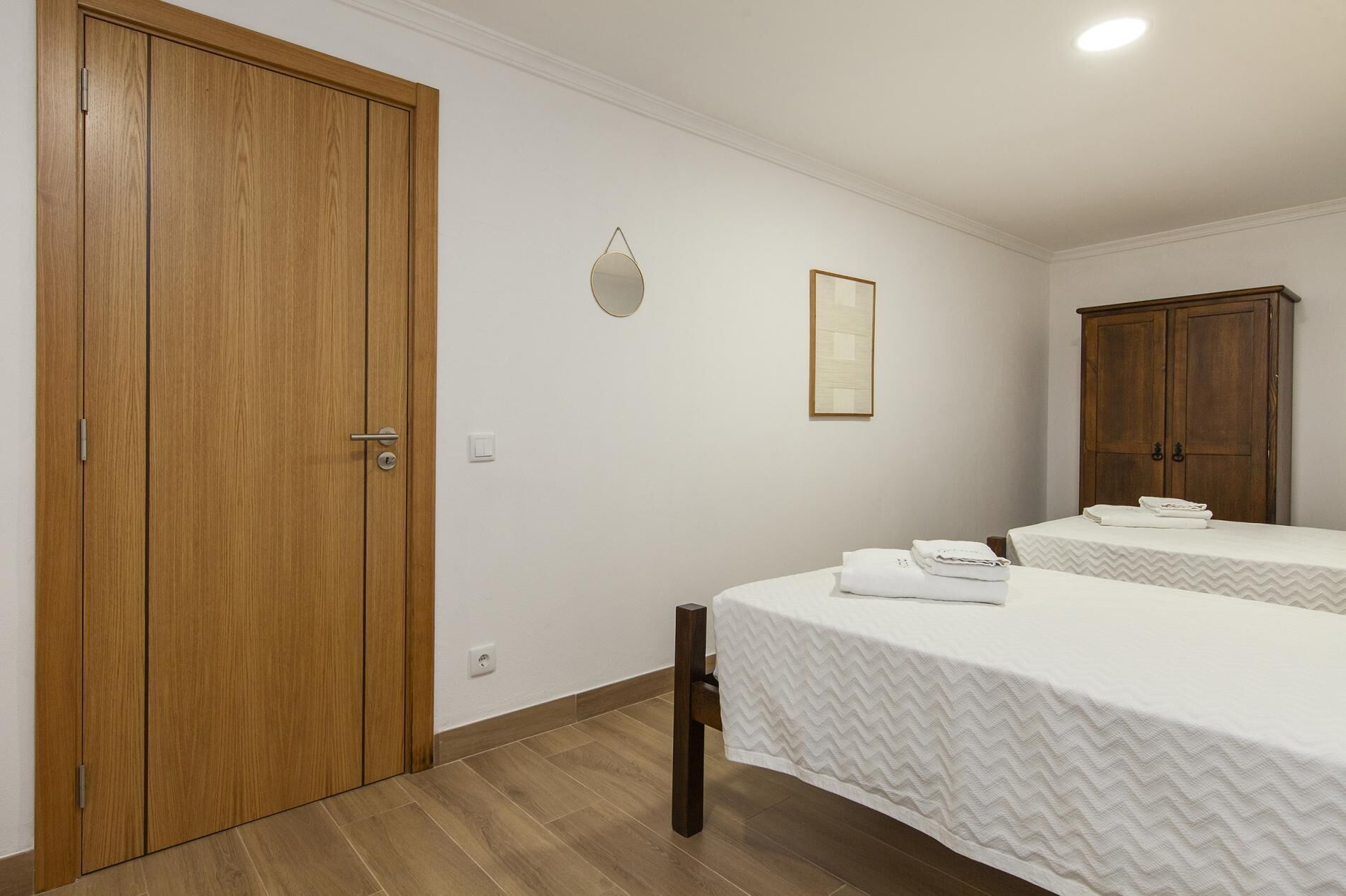 A bedroom with two beds, a wooden wardrobe, a mirror, and a framed picture on the wall.