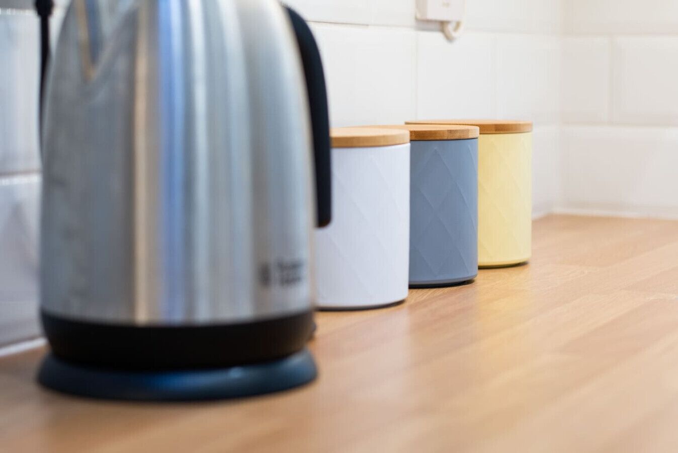 A stainless steel kettle on a wooden countertop with three containers with lids.