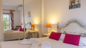 A neatly made bed with pillows, a bedside table with a lamp, a mirror, and a window with curtains. - B102 -  Sol Sol Lagos Apartment (Lagos)