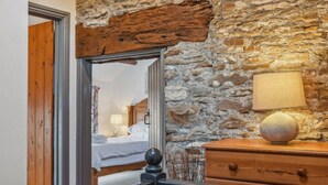 A room with a stone wall, a wooden dresser, a lamp, and a bed with a wooden headboard. - 3 Bed Cottage • Parking • Ideal for Work Trips (Pontardawe)
