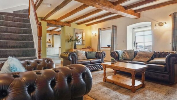 A spacious living room with a staircase, leather sofas, a wooden coffee table, and exposed wooden beams on the ceiling. - 3 Bed Cottage • Parking • Ideal for Work Trips (Pontardawe)