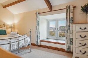 Un dormitorio con cama, cómoda, ventana con cortinas y lámpara.