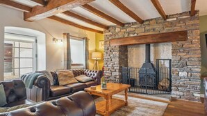 A cozy living room with a stone fireplace, leather sofa, and a wooden coffee table. - 3 Bed Cottage • Parking • Ideal for Work Trips (Pontardawe)