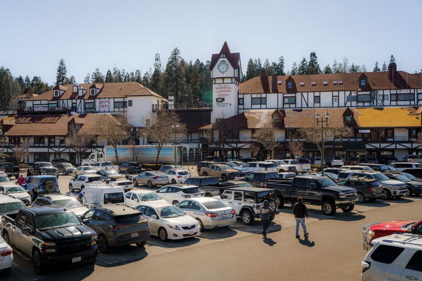 A parking lot with various vehicles, a clock tower, and buildings with signage.