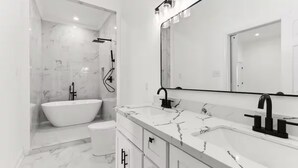 Une salle de bain moderne avec une baignoire sur pieds, un meuble-lavabo doté d’un grand miroir et un revêtement de sol en marbre.