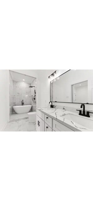 Ein modernes Badezimmer mit einer freistehenden Badewanne, einem Waschtisch mit großem Spiegel und Marmorböden.