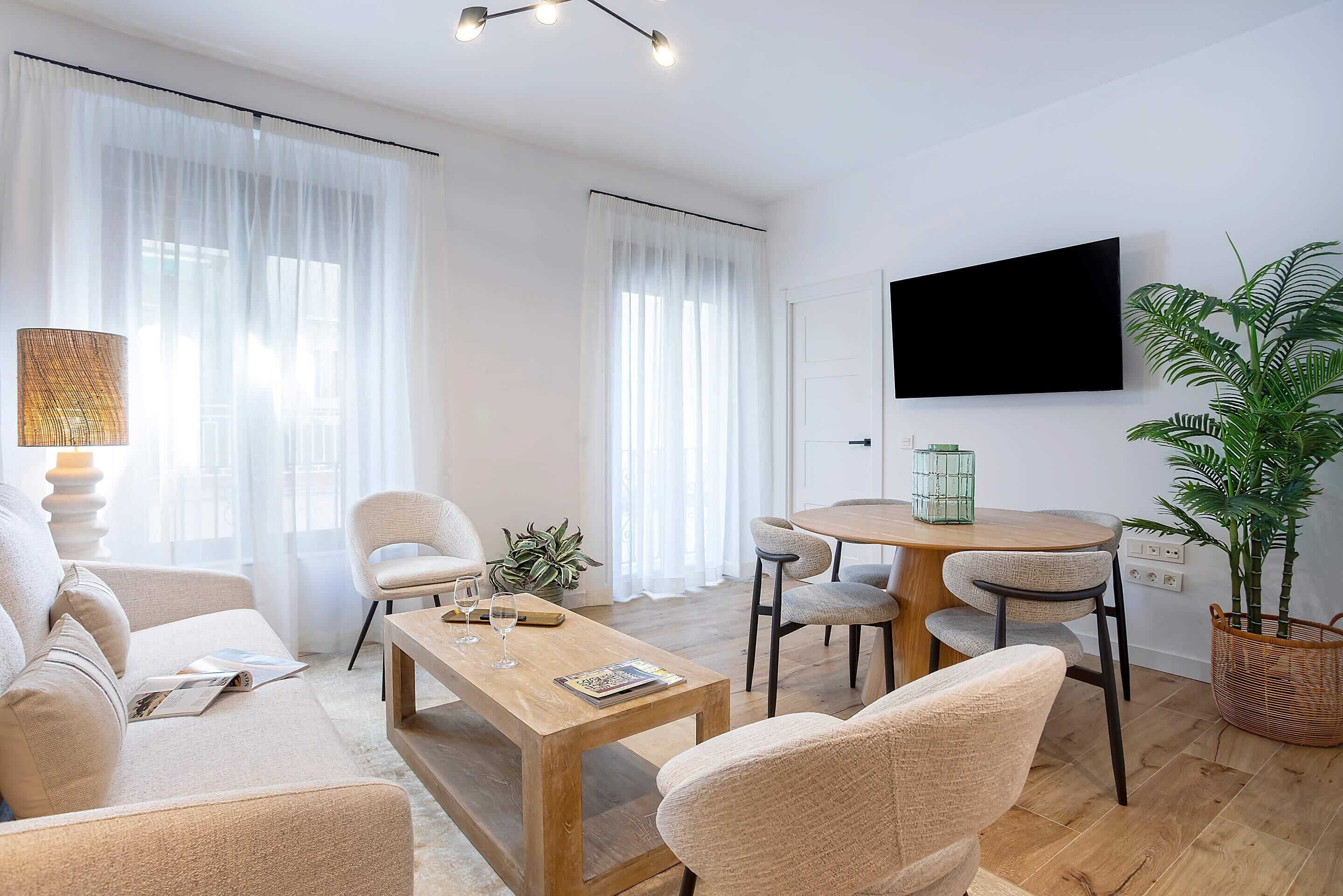 Ein modernes Wohnzimmer mit einer Couch, einem Couchtisch, Sesseln, einem Fernseher und einem Esstisch.