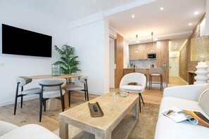 Un salon moderne avec une table basse en bois, un téléviseur fixé au mur et un espace détente comprenant un canapé et des fauteuils.