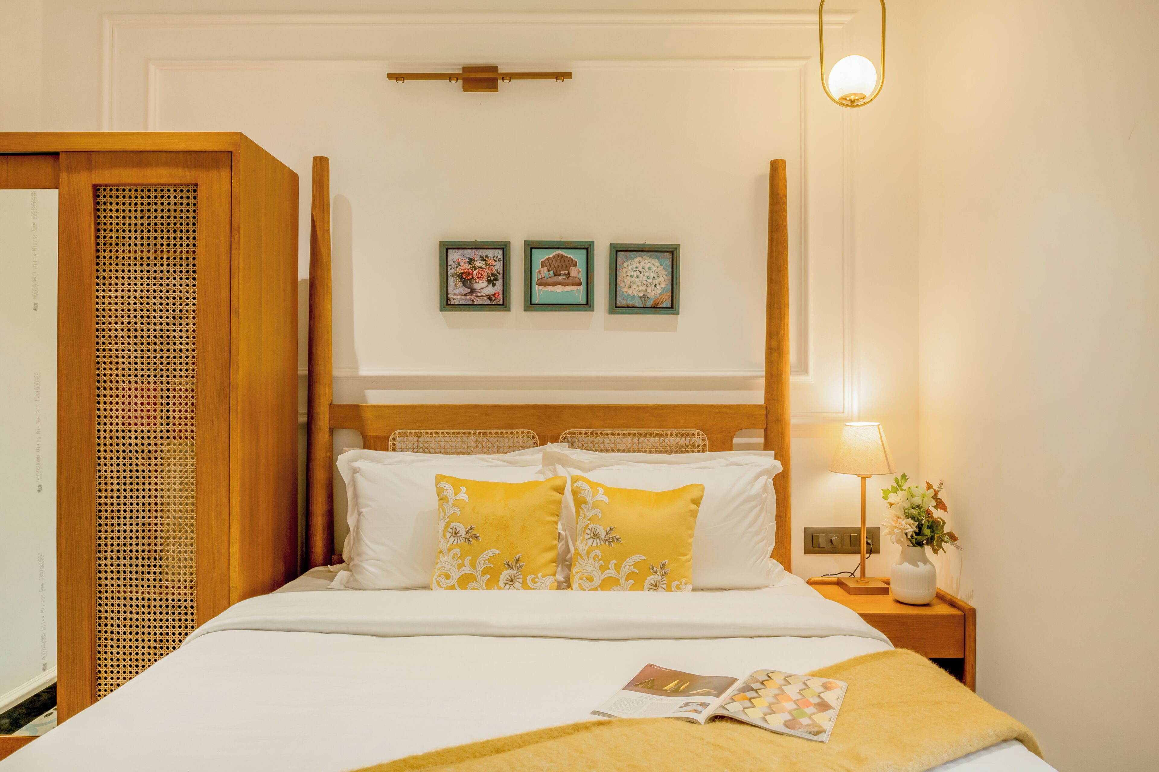 A hotel room with a bed, a nightstand with a lamp, and three framed pictures on the wall.