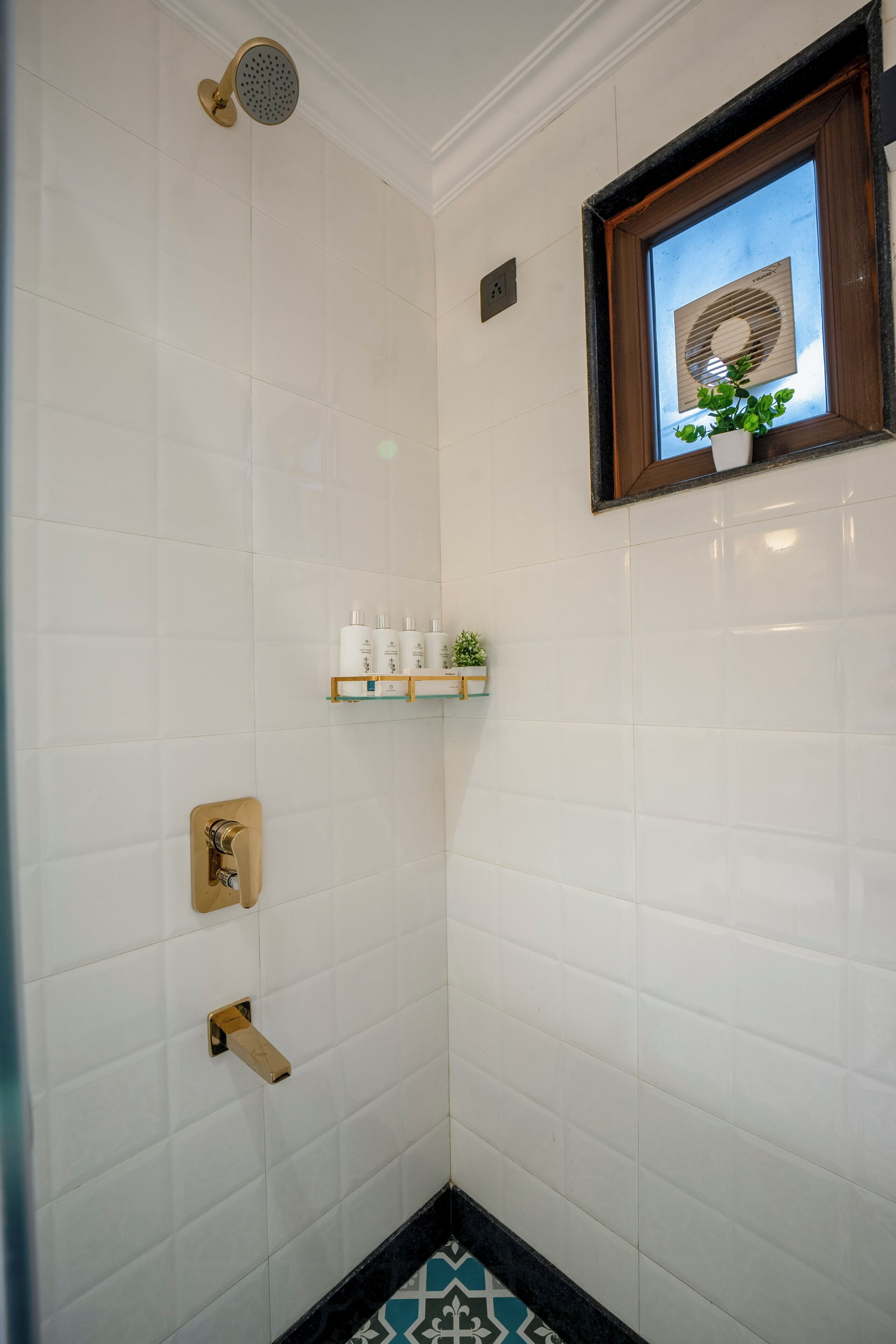 Eine Dusche mit goldfarbener Duschbrause, ein kleines Regal mit Pflegeprodukten und ein gerahmtes Bild an der Wand.